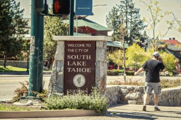 06_01 2021 South Lake Tahoe USA - Sign Welcome to South Lake Tahloe California on stree corner with man in shorts on phone walking away - movement blur.