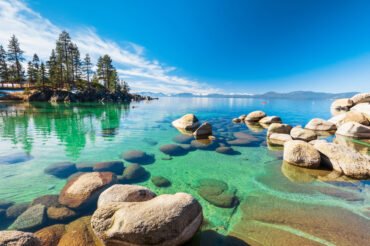Lake Tahoe rocky shoreline in sunny day, beach with blue sky ove